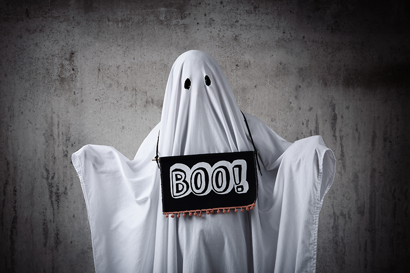 Person wearing a sheet ghost costume with a boo sign