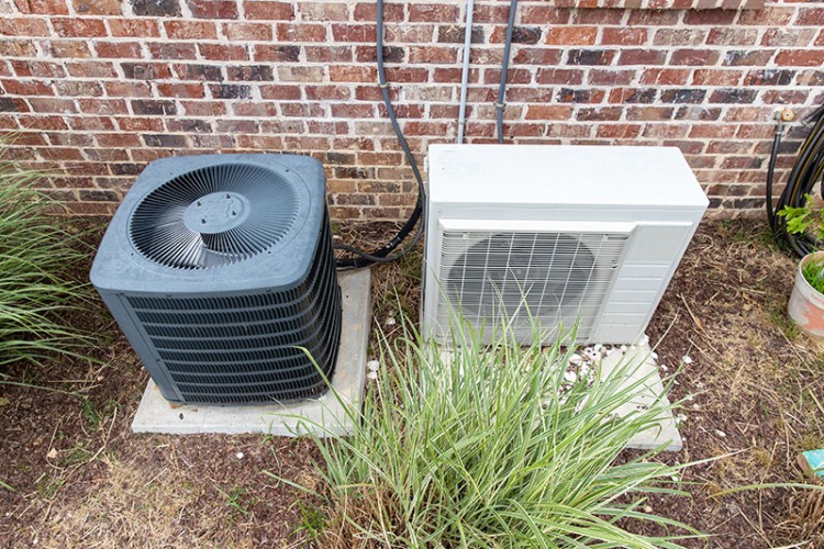 Outdoor split AC system beside a brick wall.