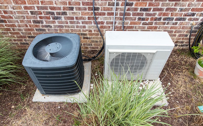 Outdoor split AC system beside a brick wall.