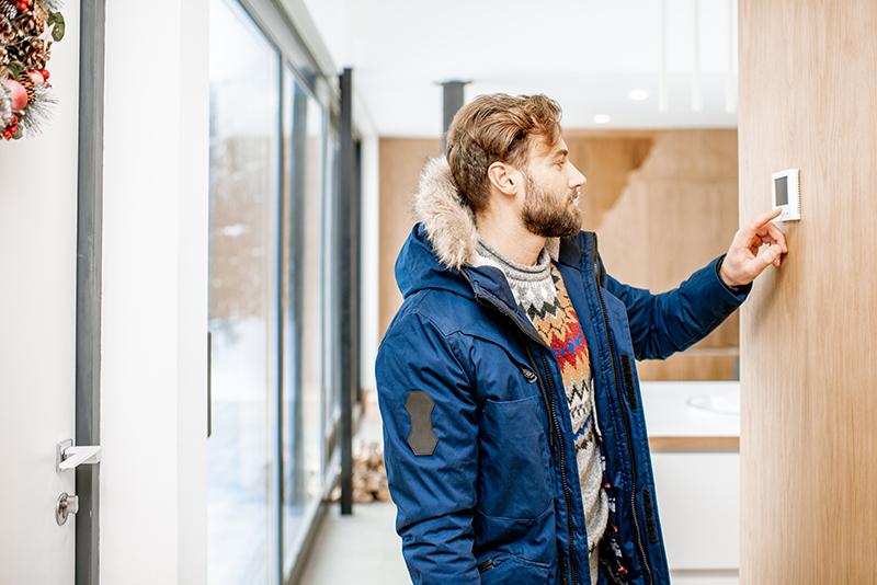 Man in a winter coat adjusting thermostat.