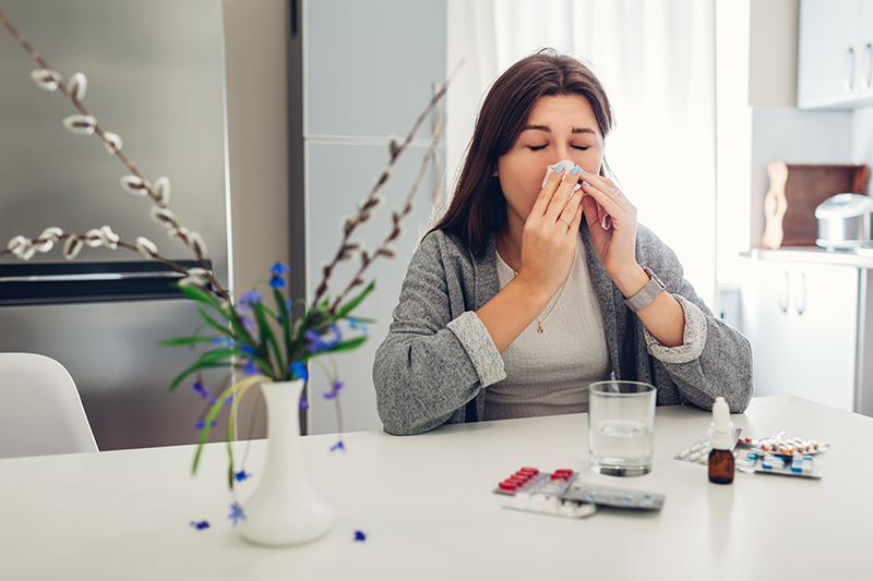 Woman sitting at a table sneezing into a tissue.