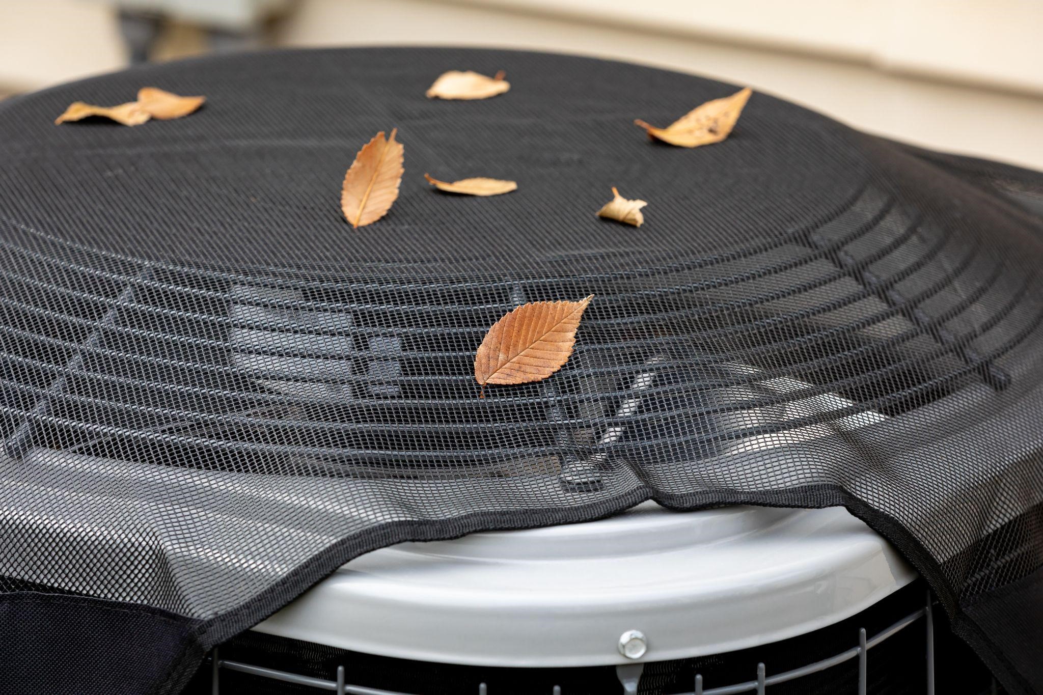 Outdoor HVAC unit covered with a protective mesh and fallen autumn leaves.
